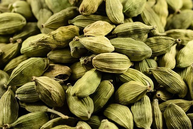 Close-up of numerous whole green cardamom pods displaying their characteristic elongated oval shape with vertical ridges, ranging in color from pale sage to deep olive green, densely arranged to show their natural dried texture and three-lobed structure